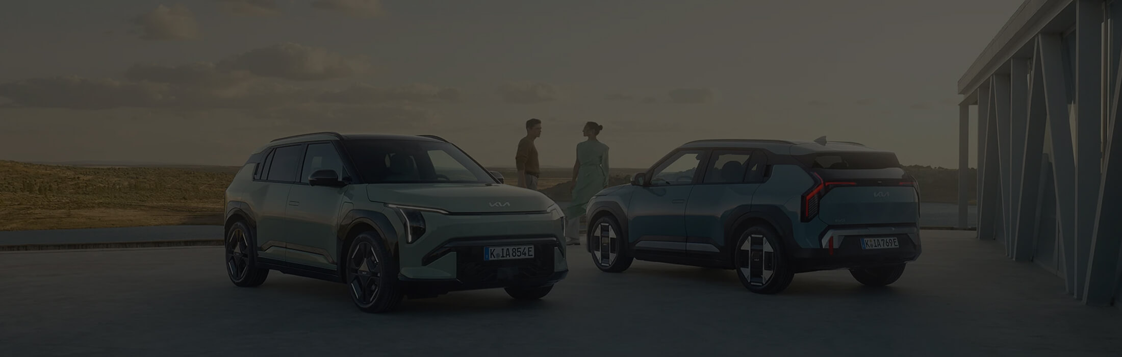 as Bild zeigt zwei Kia-Modelle: eines von vorne, das andere von hinten, mit zwei Personen in der Mitte.