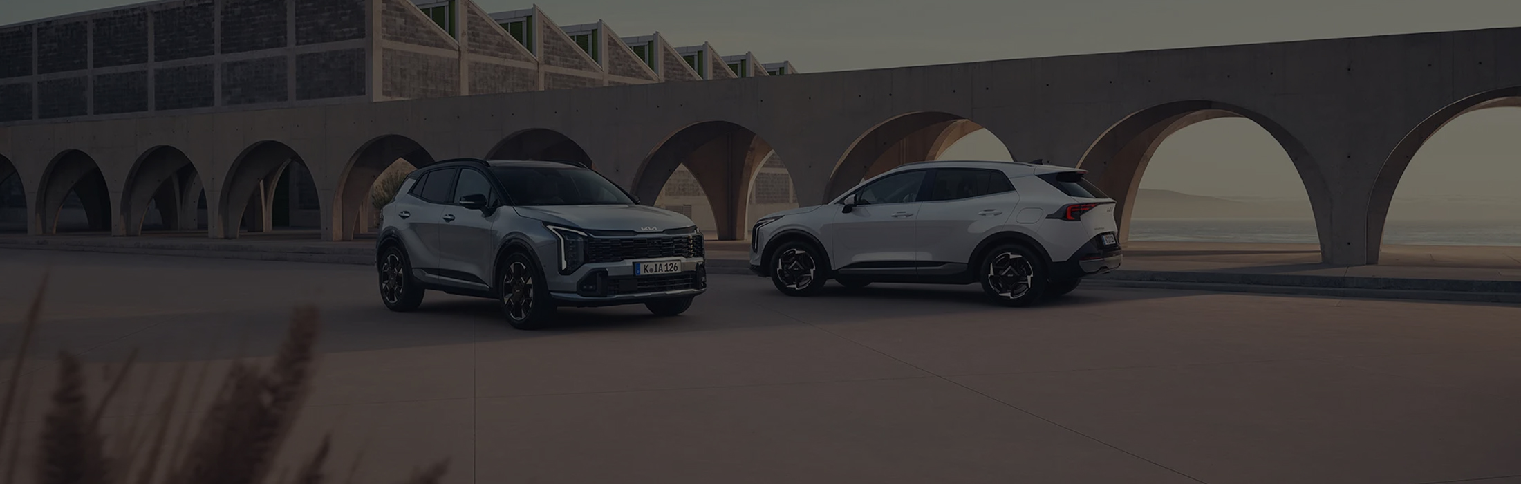 as Bild zeigt zwei Kia-Modelle: eines von vorne, das andere von hinten, mit zwei Personen in der Mitte.