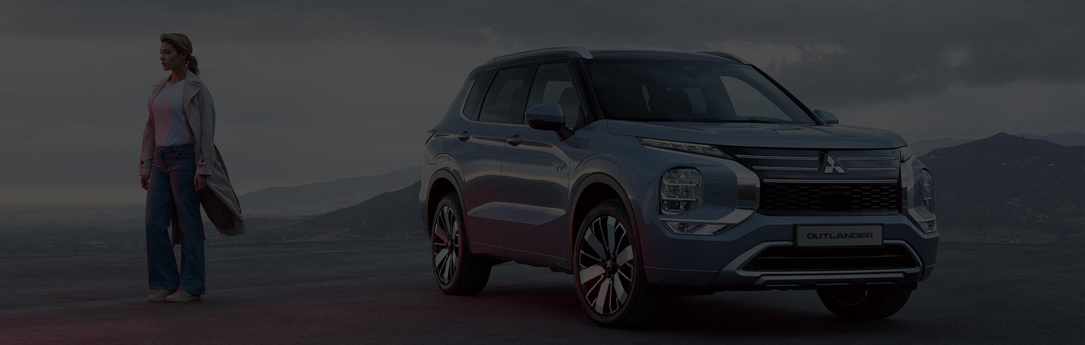 Das Bild zeigt den Mitsubishi Outlander von vorne, mit einer Frau, die in die Ferne blickt.