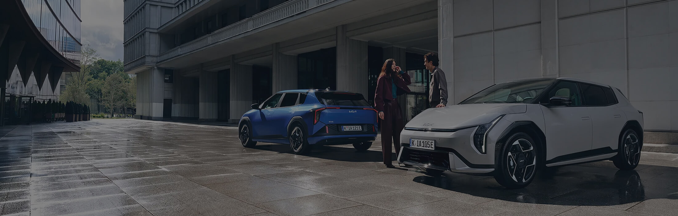 as Bild zeigt zwei Kia-Modelle: eines von vorne, das andere von hinten, mit zwei Personen in der Mitte.